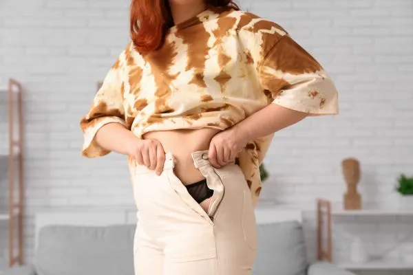 Image of woman trying to do her trousers up after pregnancy weight gain Datchet